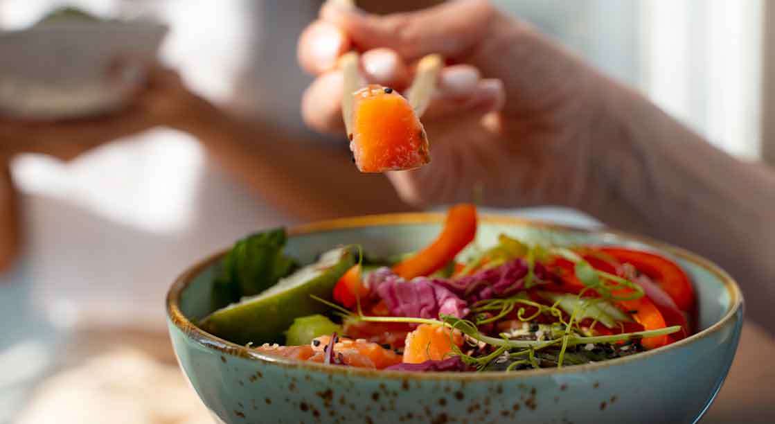 plato de verduras y salmón con mano de mujer